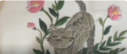 imagen de un gatito gris bordado a mano con cara feliz y rodeado de hojas y flores rosas