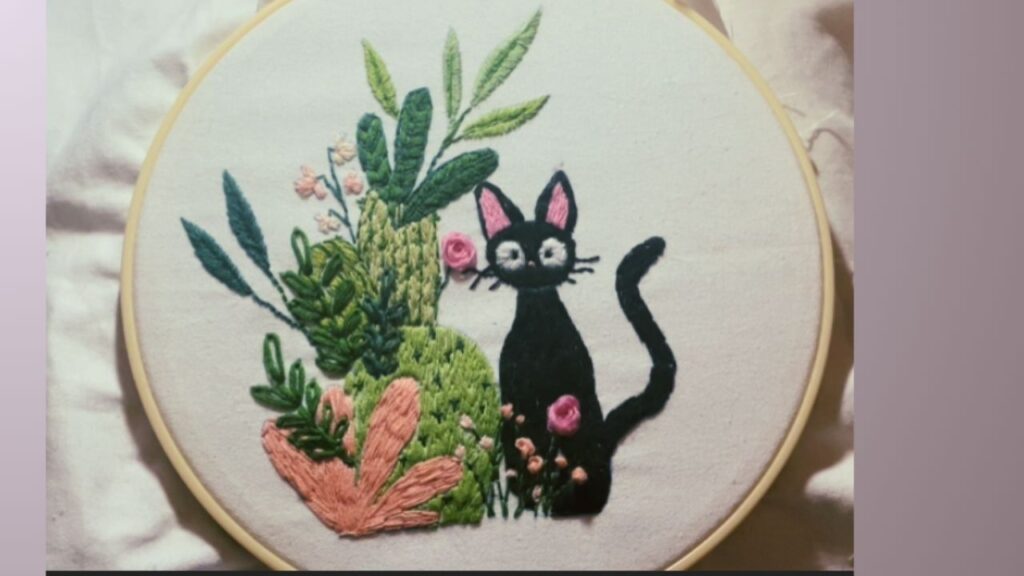 bastidor con gatito negro bordado estilo ghibli junto a cactus y flores