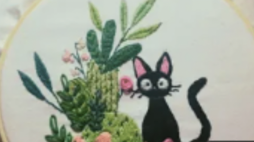 bastidor con gatito negro bordado estilo ghibli junto a cactus y flores