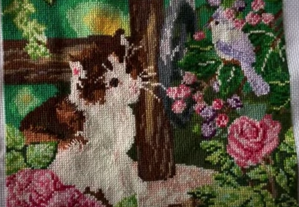 cuadro en punto de cruz terminado de un gatito romano, un pajaro violeta y flores rosas en un tronco de árbol